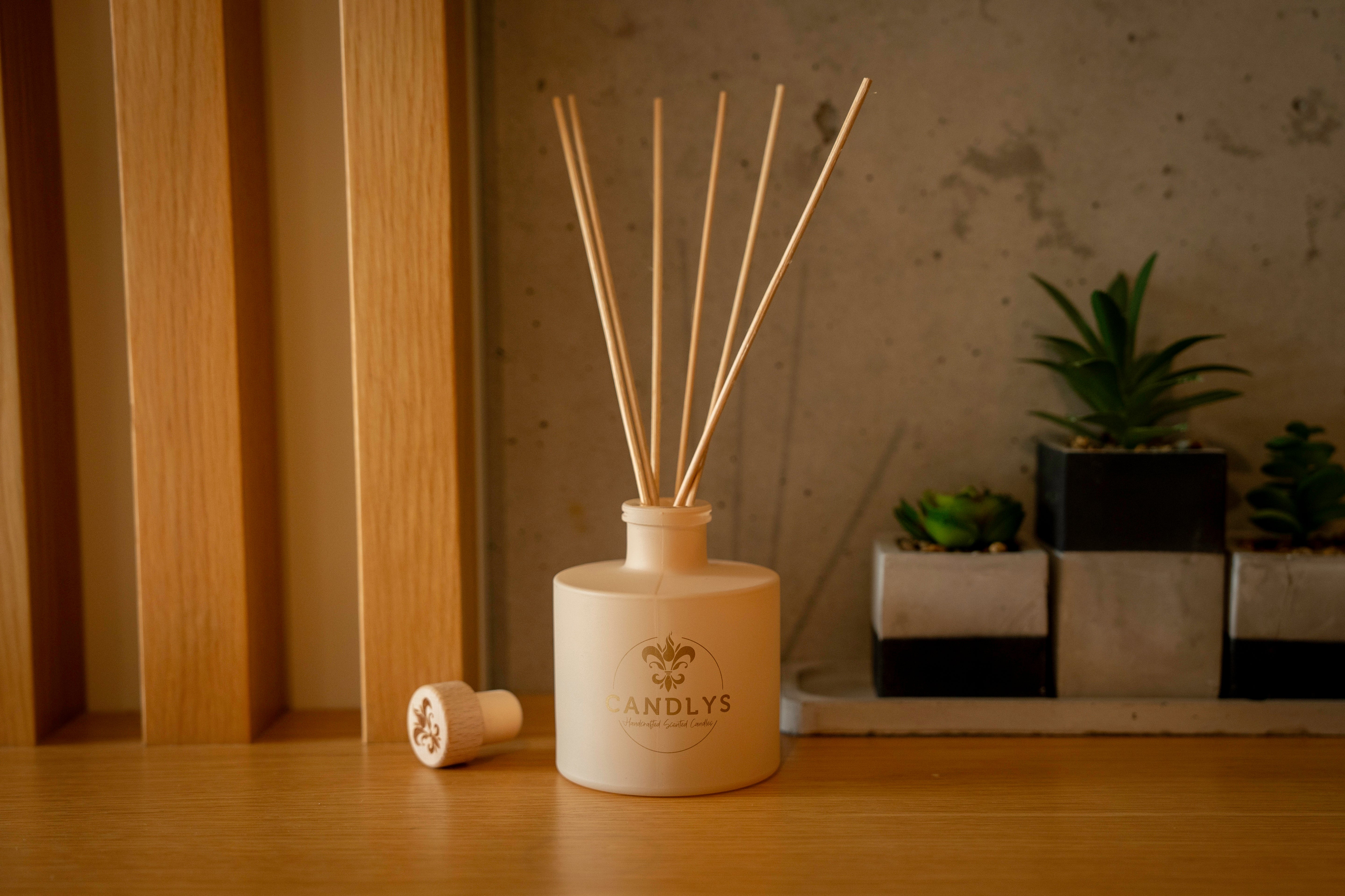 Difusor de aroma Candlys em frasco bege sobre madeira com fundo natural e plantas.