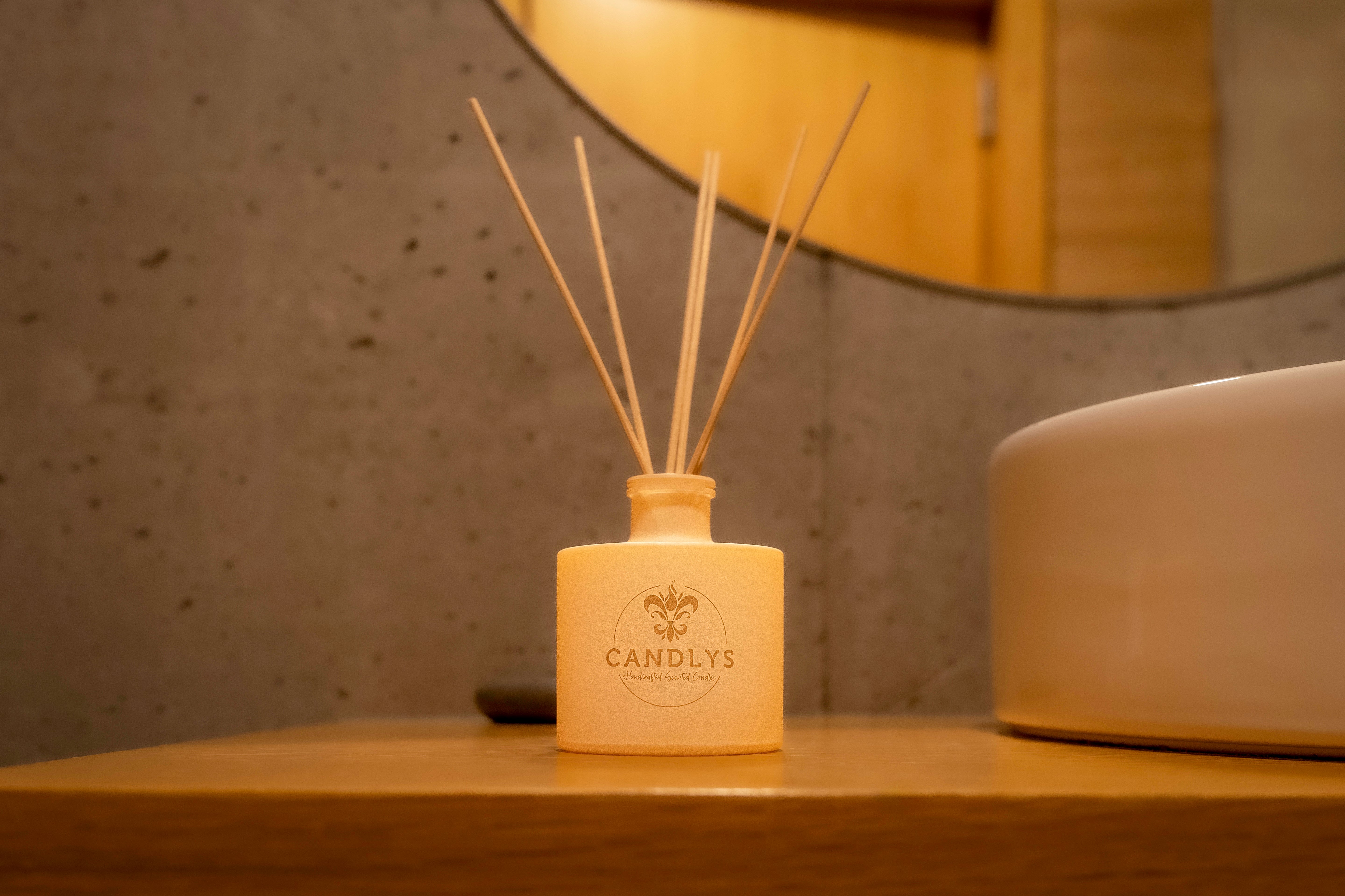 Difusor aromático da marca Candlys com varetas de madeira, sobre uma bancada de madeira numa casa de banho com decoração minimalista.