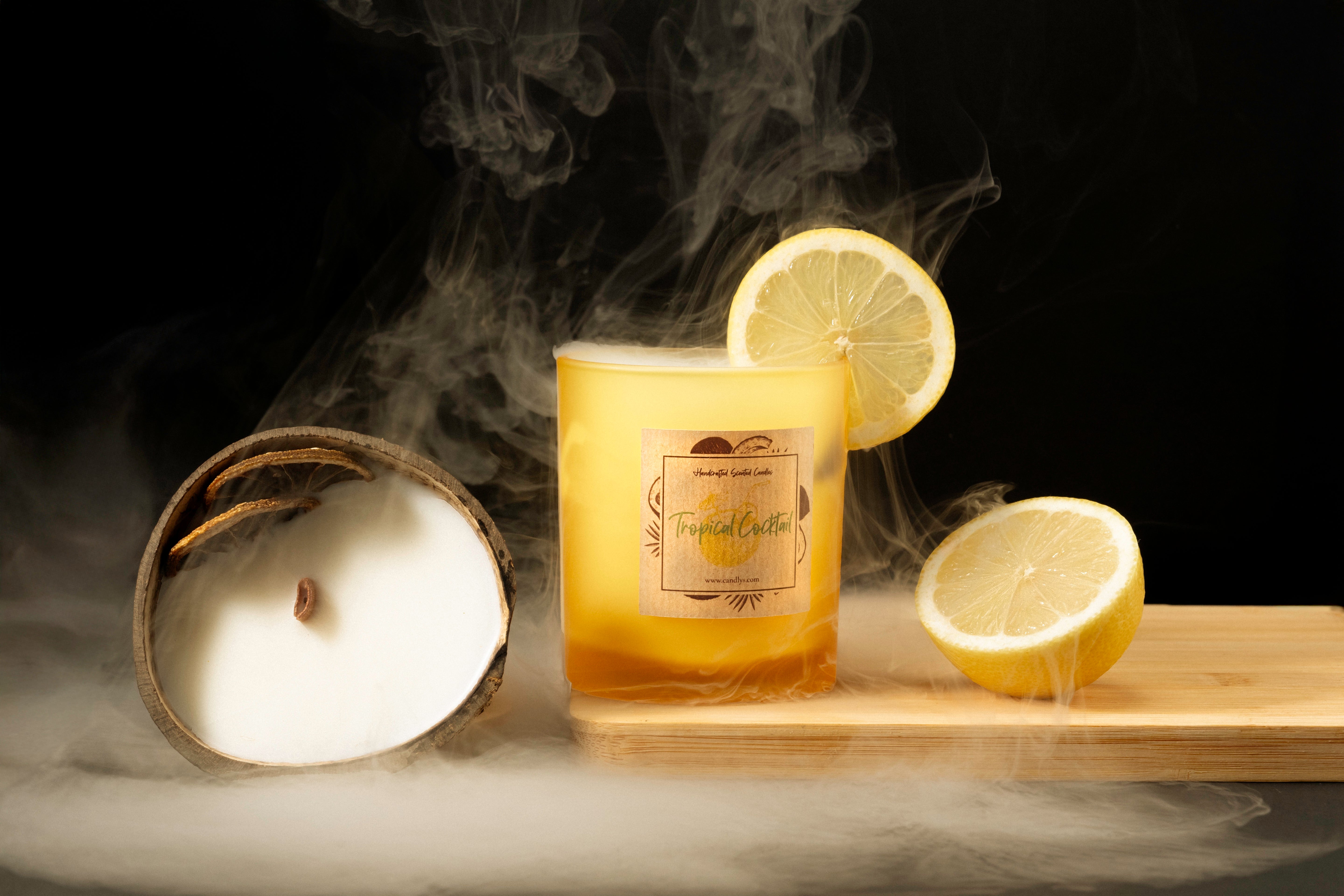 Vela Tropical Cocktail em copo amarelo mate, com coco aberto, rodelas de limão e fumo decorativo, criando ambiente tropical e intenso.
