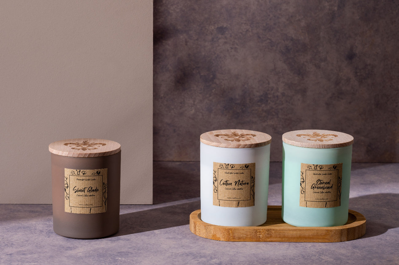 Três velas aromáticas artesanais da Candlys com tampas de madeira gravadas e rótulos em papel kraft, apresentadas sobre base de madeira em fundo minimalista.