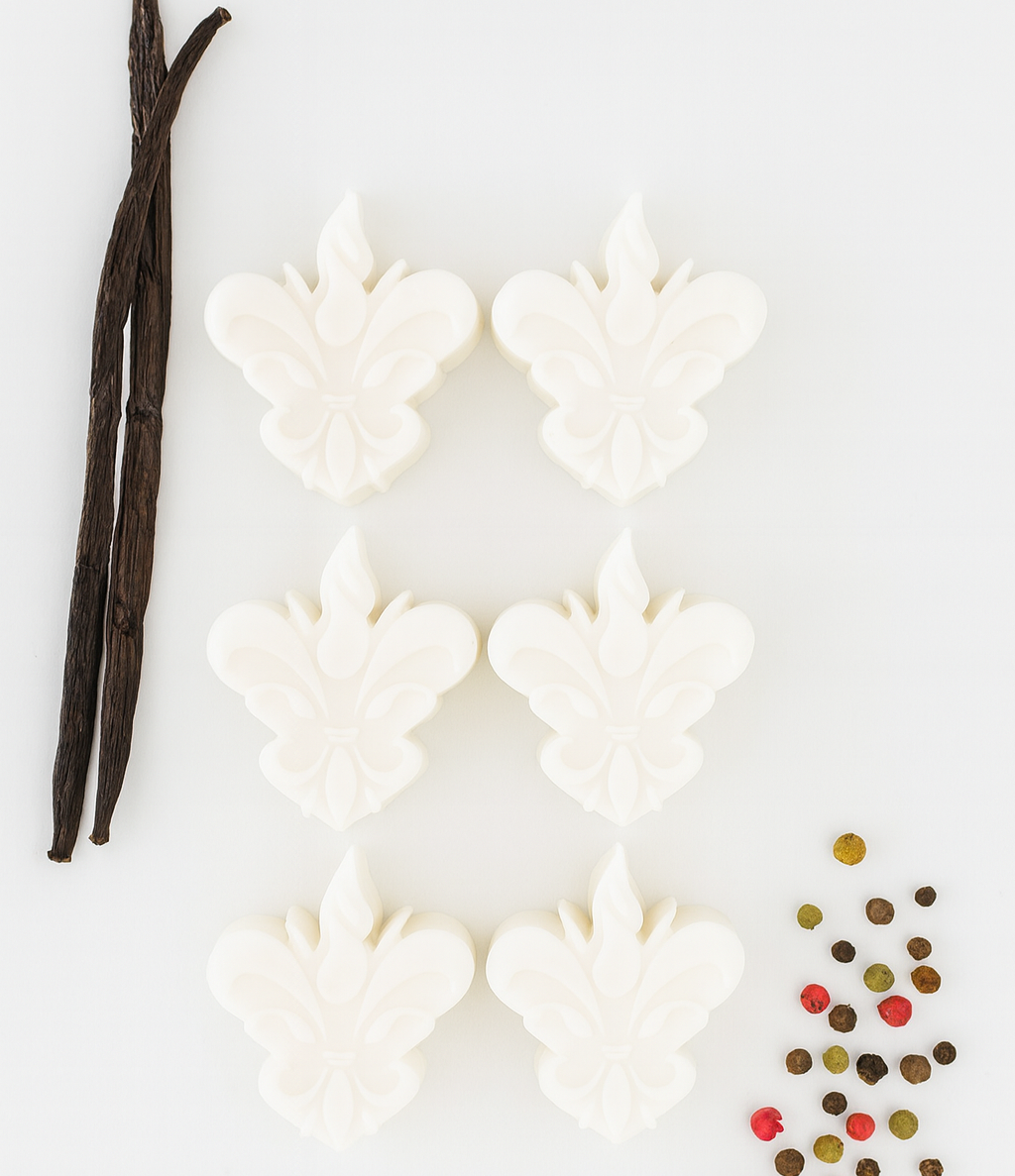 Pack de 6 wax melts brancos em forma de flor-de-lis, dispostos num fundo clean com dois paus de baunilha e várias especiarias coloridas. Edição especial da Candlys com aroma a baunilha e especiarias.