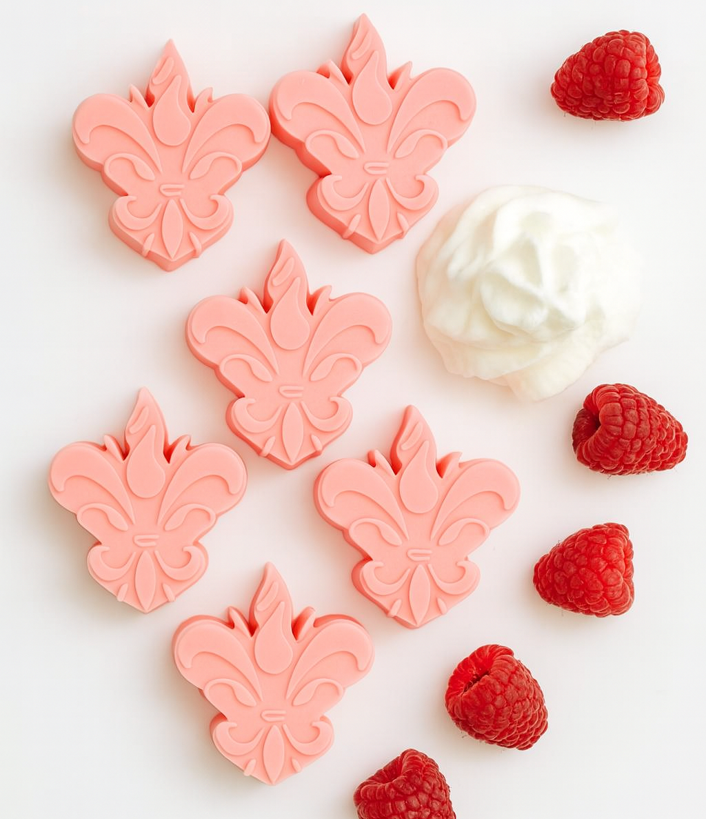 Pack de 6 wax melts rosa em forma de flor de lis, dispostos num cenário clean com chantilly e framboesas frescas ao redor — edição especial da Candlys com aroma doce e frutado.