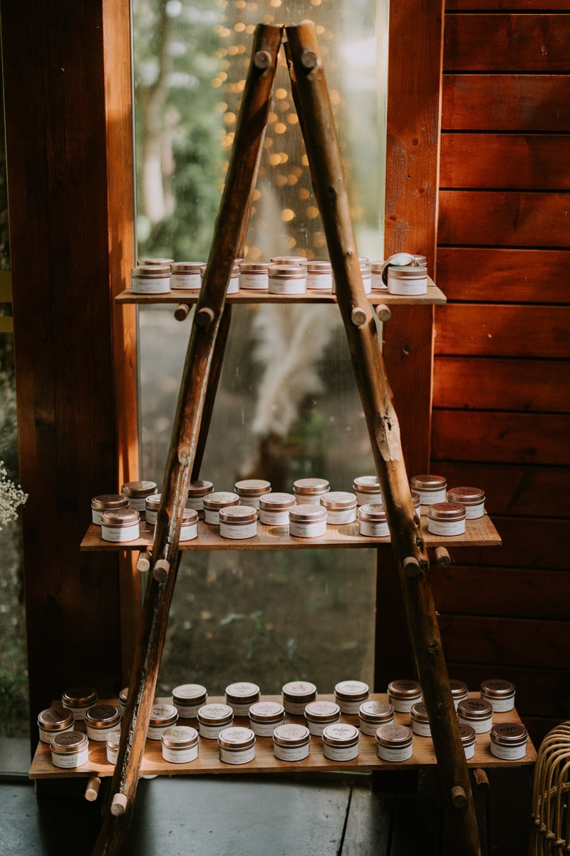 Expositor rústico em madeira com várias velas em lata Candlys organizadas em prateleiras. Velas artesanais naturais em recipientes metálicos, ideais para presentes, decoração e ambientes aromáticos.