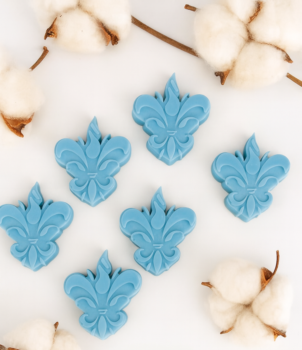 Pack de 6 wax melts Spice Crown da Candlys, em azul médio e formato flor-de-lis, apresentados num cenário clean com ramos de algodão. Fragrância: pimenta da Jamaica e patchouli. Coleção Algodão Colorido.