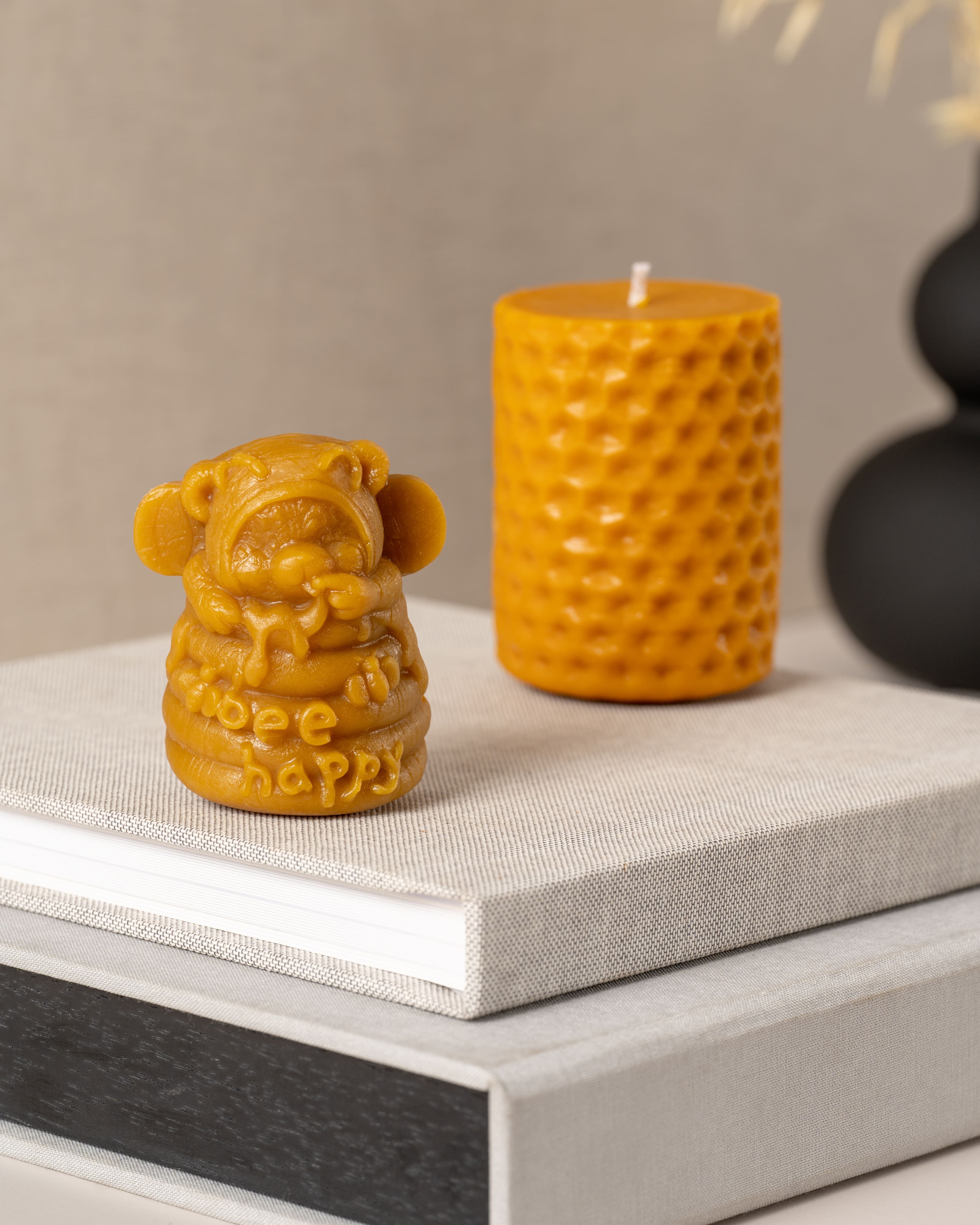 Ursinho Bee Happy em cera de abelha natural ao lado de vela cilíndrica artesanal Candlys em cera de abelha pura.