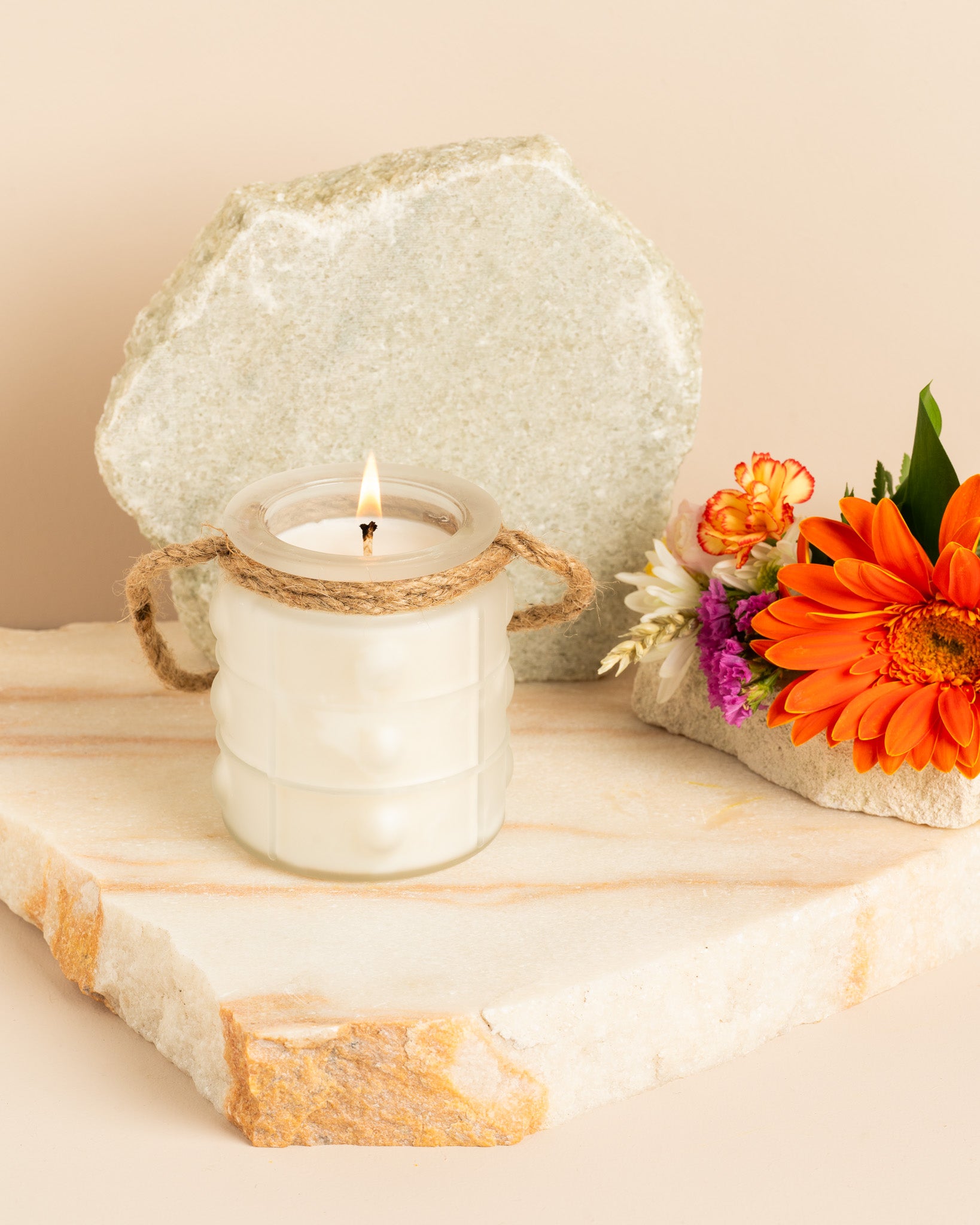 Vela aromática Brides Bouquet em copo branco com relevo suave no centro, inspirado na forma de uma pérola. Alça de corda natural e flores decorativas.