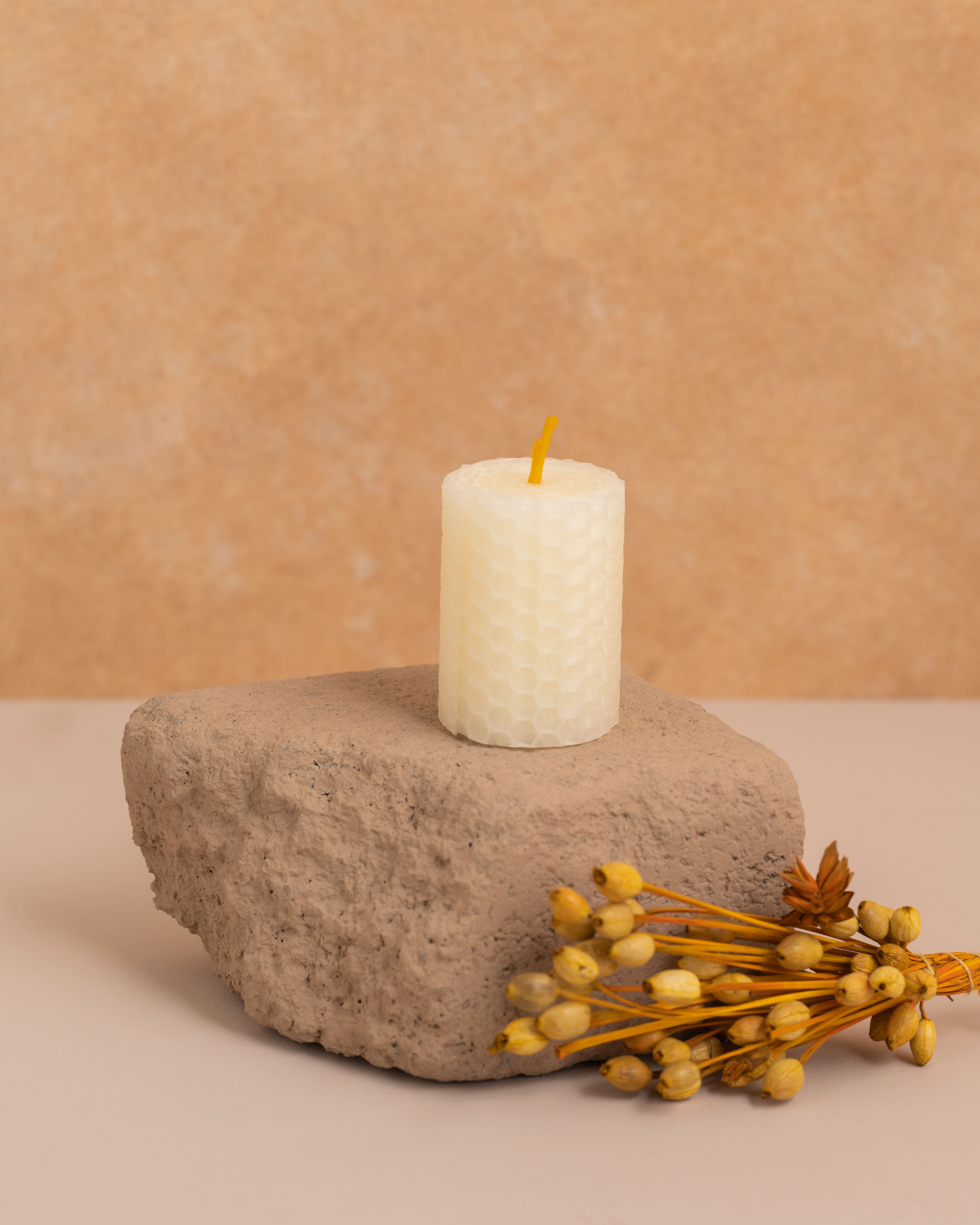 Vela artesanal em cera de abelha cor pérola branco com 5 cm de altura, feita a partir de folhas de cera enroladas. Textura hexagonal dos favos de mel em detalhe, elegante e minimalista para decorações delicadas.