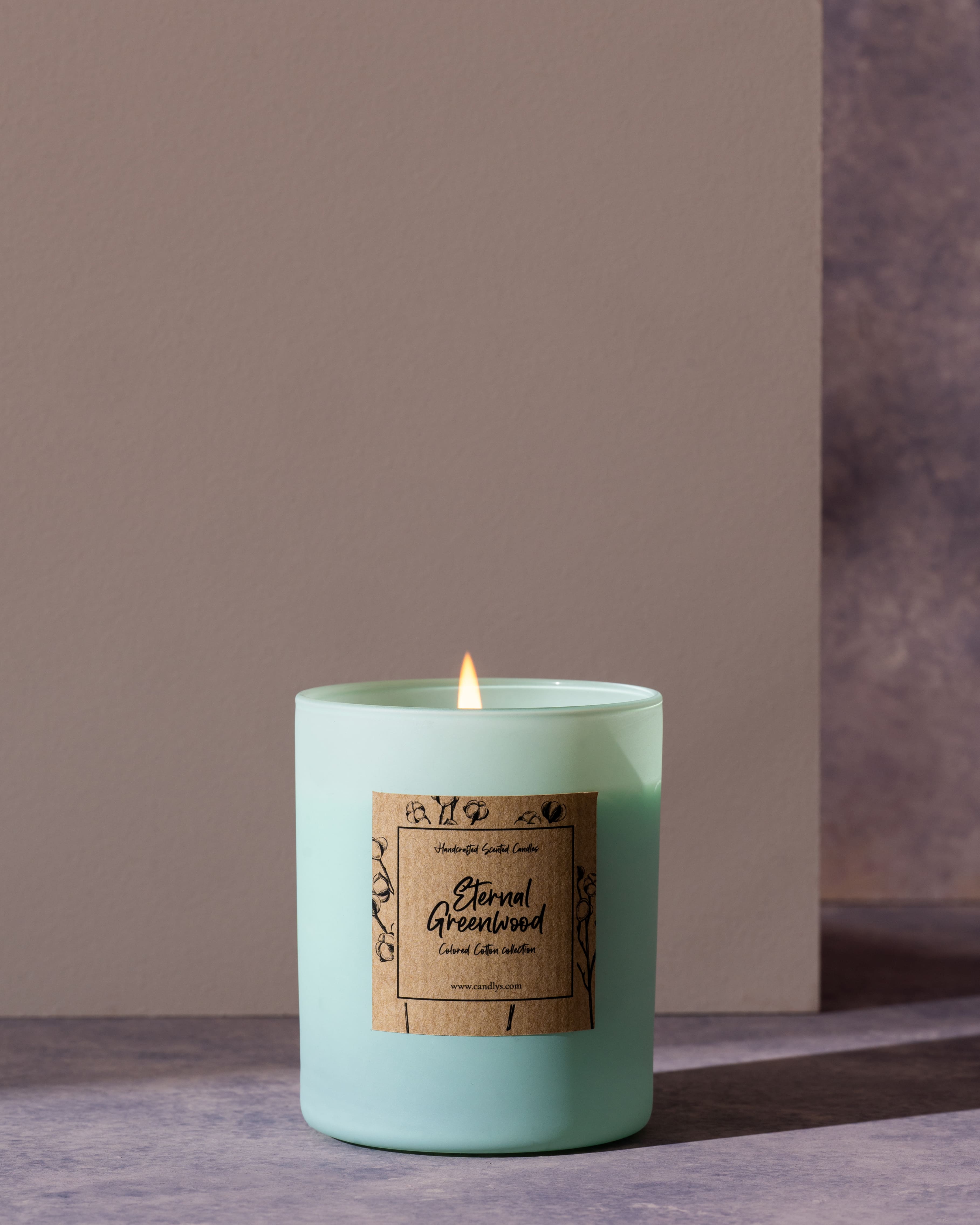 Vela Eternal Greenwood acesa em copo verde mate, colocada num cenário elegante de tons cinzentos.