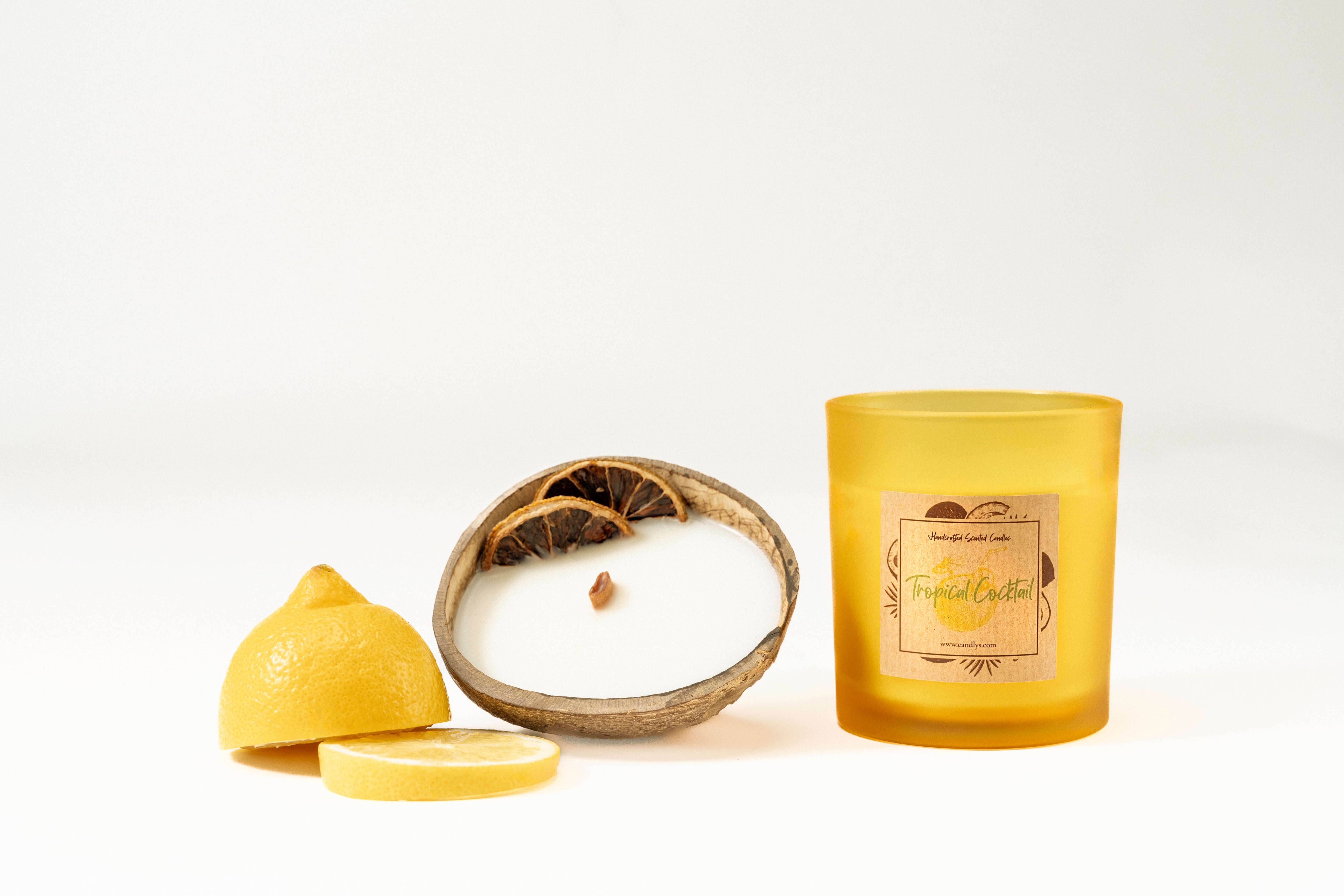 Vela Tropical Cocktail em copo amarelo mate, acompanhada por meio coco e limão decorativo, fundo branco.