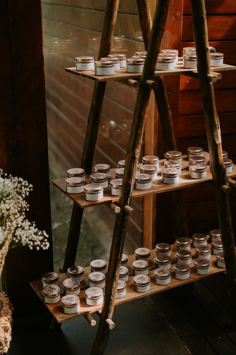 Latas metálicas com velas artesanais Candlys expostas em prateleira rústica de madeira. Velas naturais em recipientes práticos e elegantes, ideais para oferecer ou decorar com um toque sustentável.