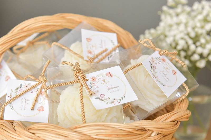 Velas artesanais Candlys em forma de flor, embaladas individualmente em caixas transparentes com etiqueta personalizada e laço de corda, apresentadas numa cesta de verga.