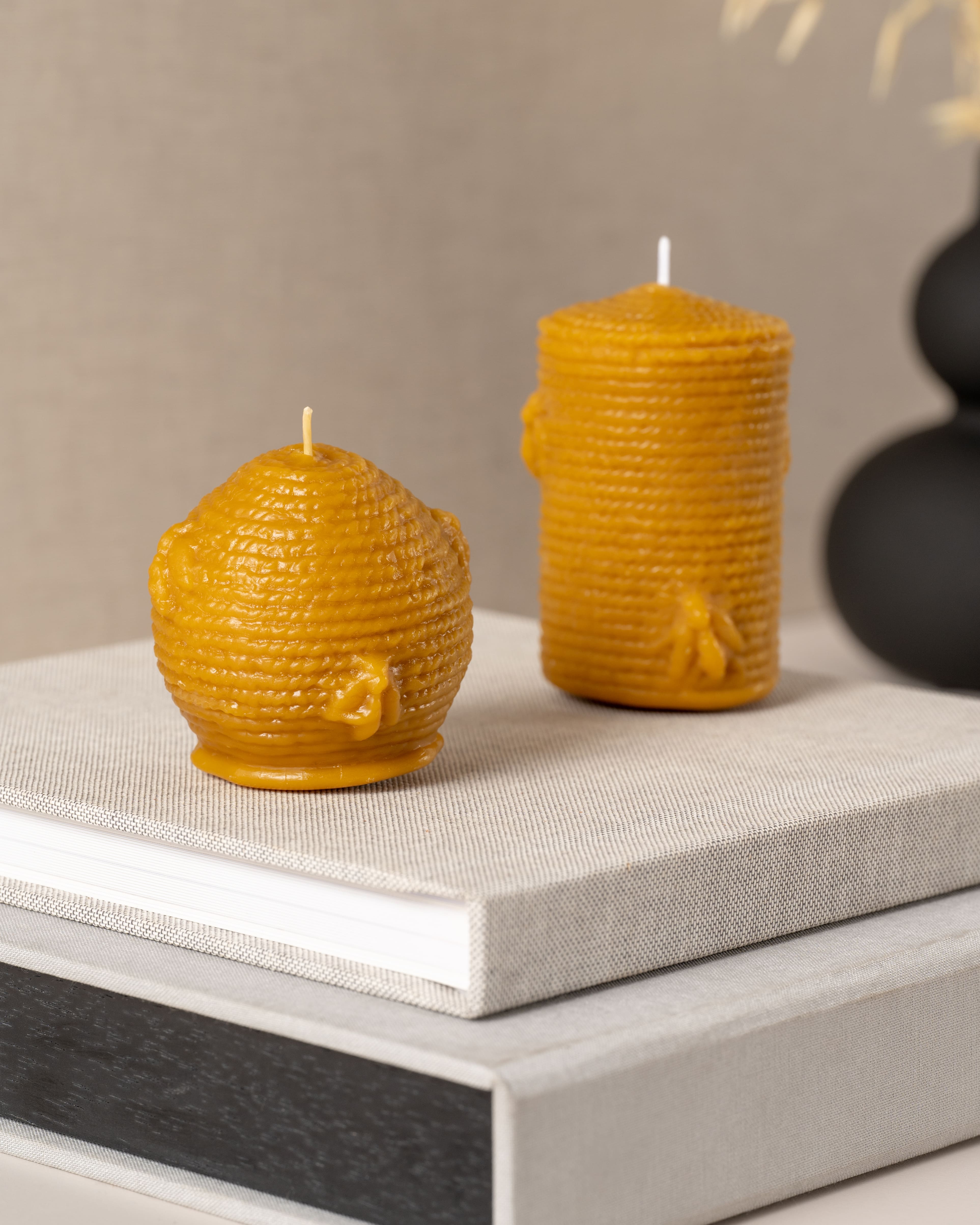 Duas velas artesanais em cera de abelha pura da Candlys: à esquerda em formato de esfera com textura de colmeia e abelha em relevo, e à direita em formato cilíndrico também inspirado em colmeia tradicional. Tons dourados naturais que realçam a autenticidade da cera de abelha.
