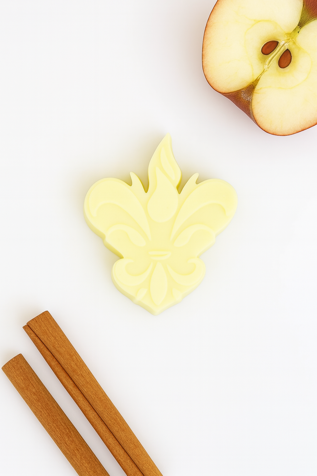 Wax melt artesanal em forma de flor-de-lis, acompanhado por paus de canela e meia maçã, representando a edição especial Maçã e Canela da Candlys.