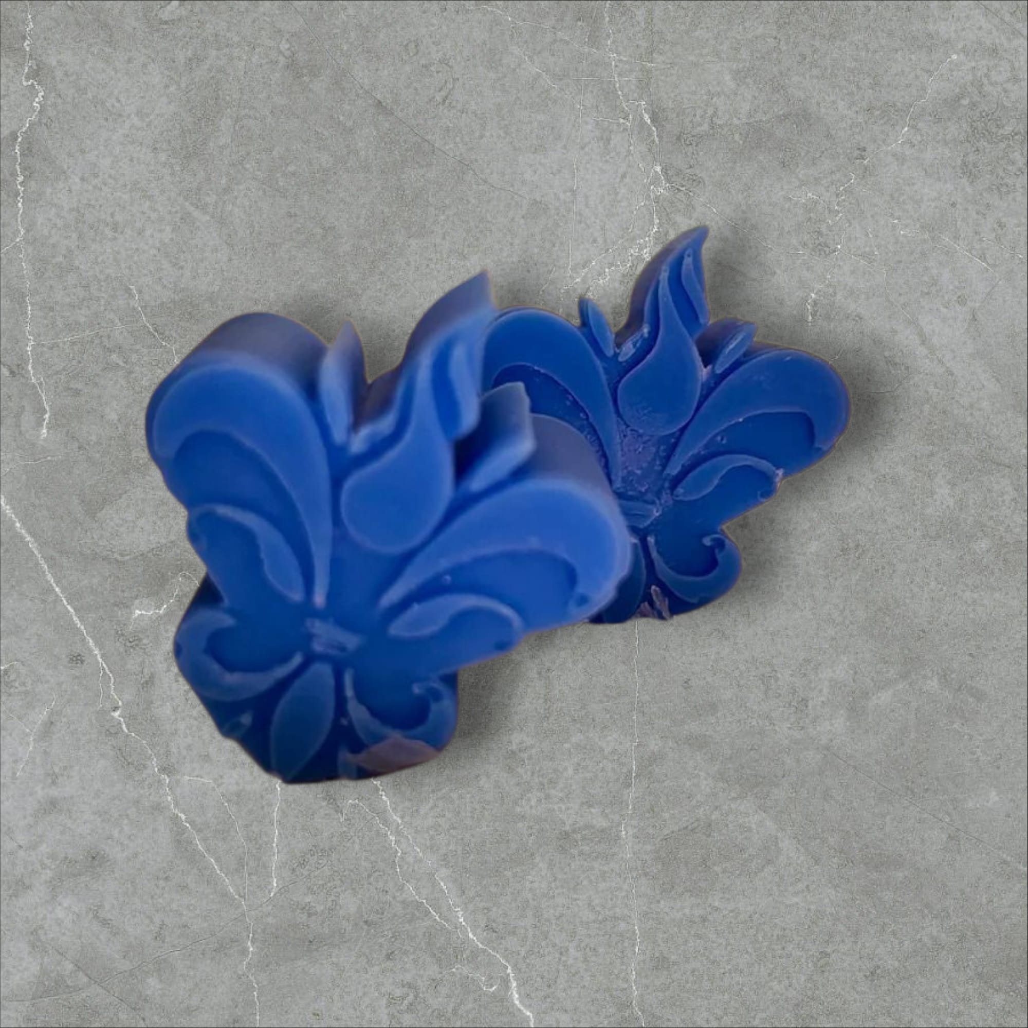 Wax melts Pimenta da Jamaica & Patchouli em tom azul-escuro, moldados em formato decorativo sobre base de pedra cinzenta, evocando uma fragrância intensa, exótica e especiada.